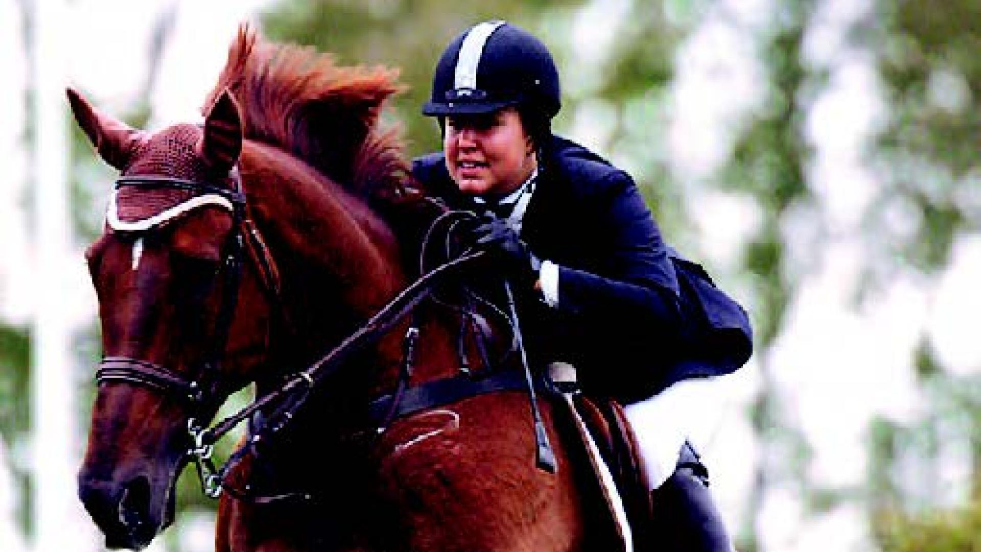 Natalie Jones rides a chestnut horse over a tall jump.